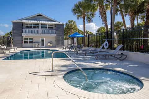 Resort pool with hot tub, lounge chairs, and beachfront house with palm trees