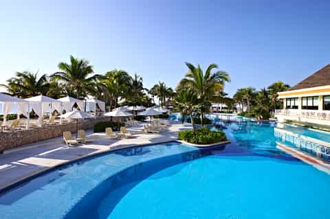 All-inclusive resort pool complex with white cabanas, palm trees, and tropical landscape
