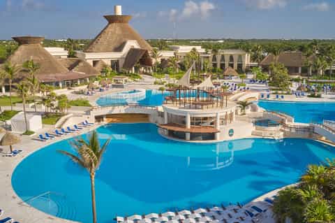 Large resort complex with massive pool, thatched-roof structures, and palm landscaping