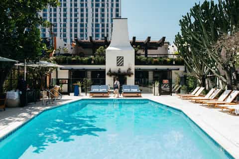 Urban rooftop pool with turquoise water, lounge chairs, modern building, and city views