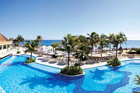 Tropical all-inclusive resort pool complex with palm trees, ocean view, and beach access
