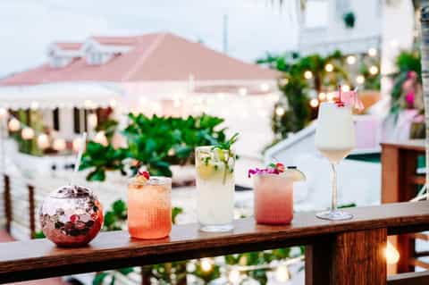 Colorful cocktails on table with pool, umbrellas, and white beachfront buildings in blurred background
