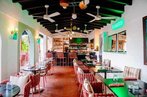 Modern restaurant interior with colorful ceiling details, bar, dining tables, and neon signage
