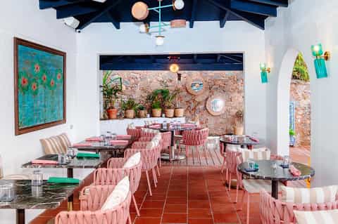 Colorful outdoor restaurant with pink chairs, cork walls, and Mediterranean architectural details