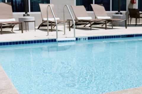 Clean swimming pool with ladder and lounge chairs on concrete deck