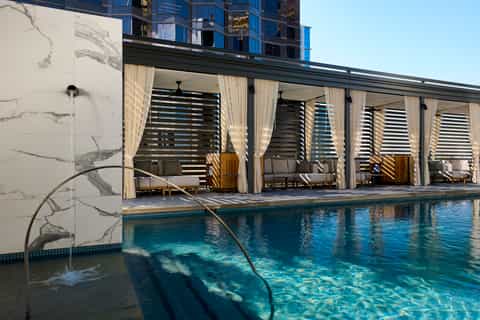 Modern rooftop pool with draped cabanas, marble walls, and city skyline views from urban resort