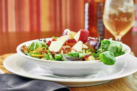 Elegant salad with mixed greens, apples, walnuts, and cheese paired with wine at upscale dining