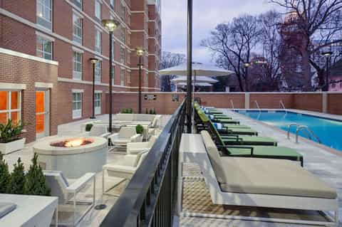 Hotel pool deck with fire pit seating, loungers, and residential brick building
