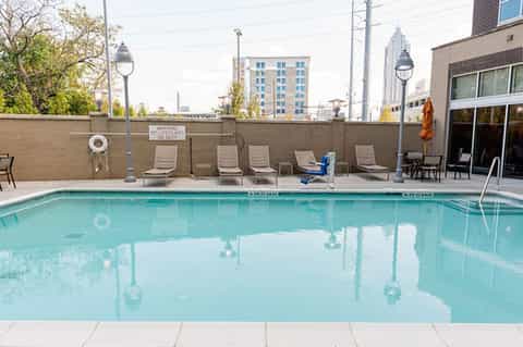 Urban rooftop pool with lounge chairs, brick wall, and city skyline views