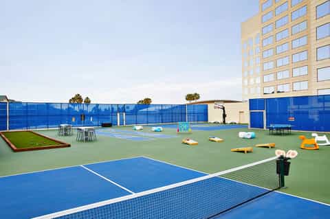 Rooftop recreational facility with tennis courts, fitness equipment, and blue safety barriers