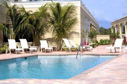 Resort pool with palm trees, white lounge chairs, classical architecture, and tropical landscaping
