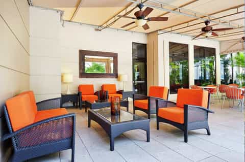 Covered outdoor lounge area with orange cushioned chairs and dark rattan furniture