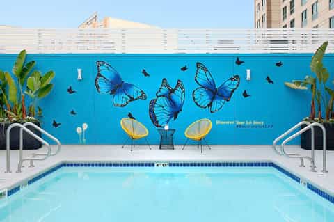 Resort pool with blue butterfly mural, yellow lounge chairs, and white fence backdrop