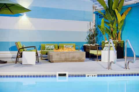 Resort poolside patio with blue striped walls, lounge chairs, fire pit, and tropical plants