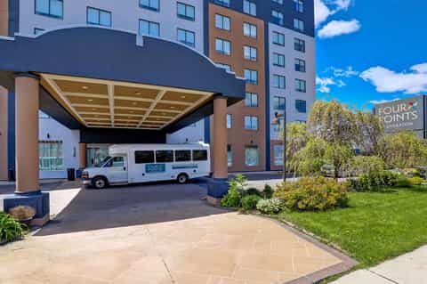 Hotel entrance with modern building, shuttle van, and landscaped grounds