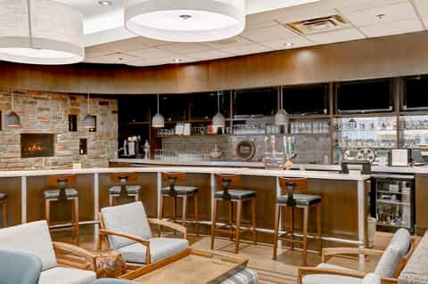 Hotel bar lounge with stone fireplace, pendant lighting, bar seating, and ambient wood finishes