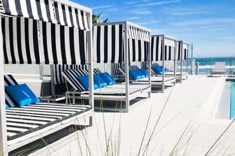 Row of striped beach cabanas with blue cushions and white frames along a sunny coastal deck