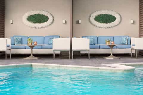 Modern pool area with white wicker loungers, blue cushions, decorative wall art, and water feature