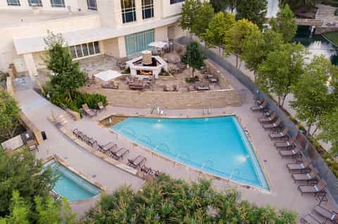 Aerial view of resort pool with lounge chairs, fire pit, and hotel building surrounded by trees