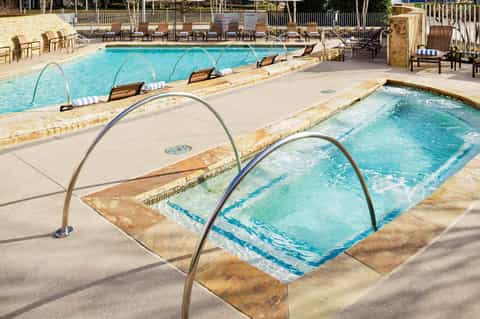 Resort pool area with multiple hot tubs, lounge chairs, and wooden fencing