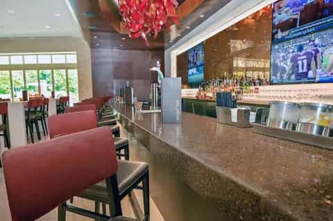 Hotel bar with red pendant light, sports TVs on walls, burgundy seating, and full liquor bottles