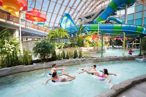 Indoor water park with tropical plants, colorful water slides, and children playing in shallow pools