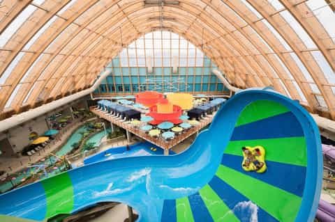 Indoor water park with blue spiral slide, wooden dome ceiling, and colorful activity areas visible below