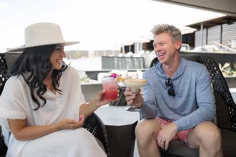 Couple toasting colorful tropical drinks on rooftop terrace with city view in casual resort attire