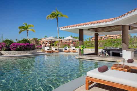Luxury resort pool with crystal clear water, cabanas, palm trees, magenta bougainvillea, and mountain views