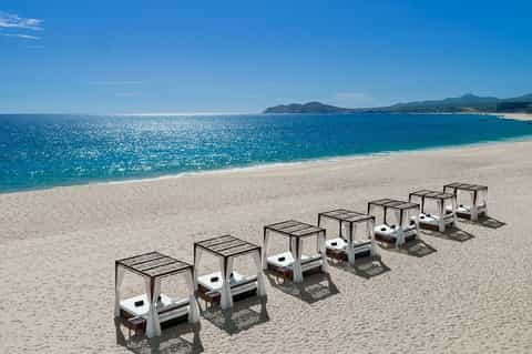 Row of white beach cabanas with black canopies on pristine sand overlooking turquoise ocean