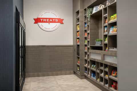 Hotel treats shop with 'TREATS' sign, stocked shelving, and vending machine for snacks and beverages