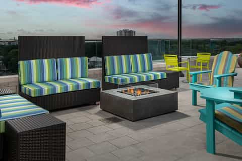 Rooftop patio with striped outdoor furniture, fire pit, and sunset sky over landscaped grounds