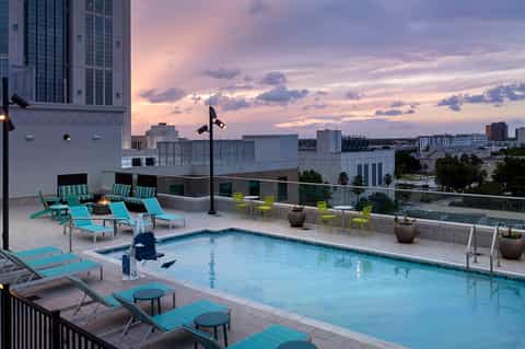 Rooftop pool at dusk with turquoise loungers and downtown city skyline at sunset
