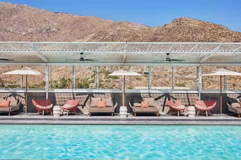 Desert resort pool with red lounge chairs under modern shade structures and mountain views