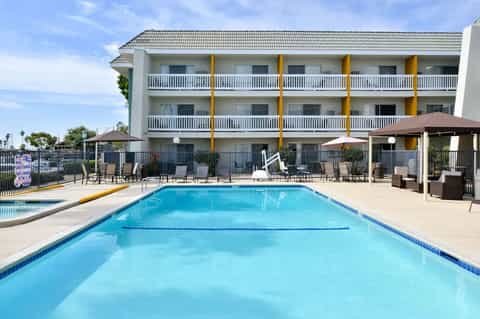 Hotel pool with blue water, lounge chairs, multi-story building with yellow columns, umbrella