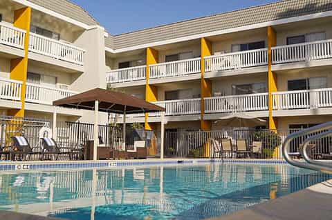 Resort courtyard with curved pool, bright yellow architectural accents, multi-story balconies, umbrellas