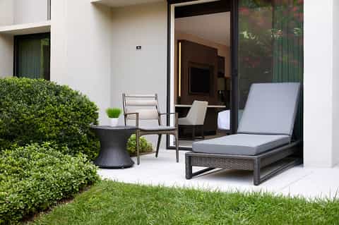 Modern patio with black rattan lounger, chair, side table, and manicured hedges