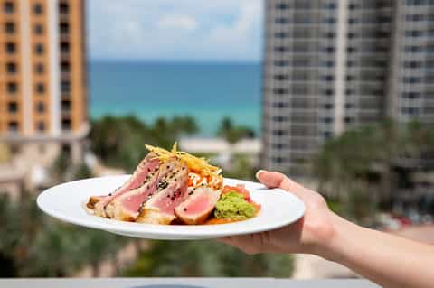 Seared tuna with sesame crust and avocado served on white plate with ocean view backdrop