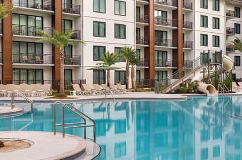 Multi-story resort building with brick and white facade, ground-level pool and tropical landscaping
