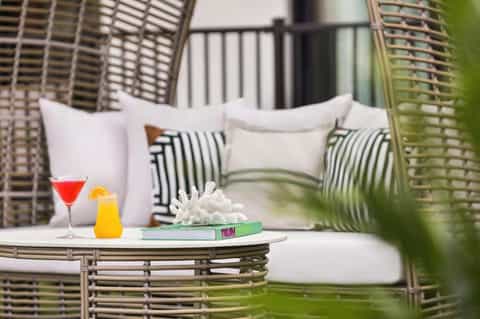 Woven lounge chairs with white pillows and small table holding cocktails in tropical setting