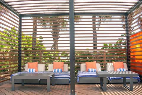 Covered outdoor lounge area with striped pergola, grey loungers with blue and white striped blankets and orange pillows