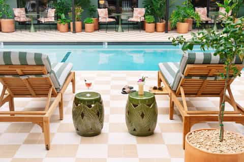 Resort pool with striped loungers, wooden deck chairs, green accent tables, and manicured landscaping