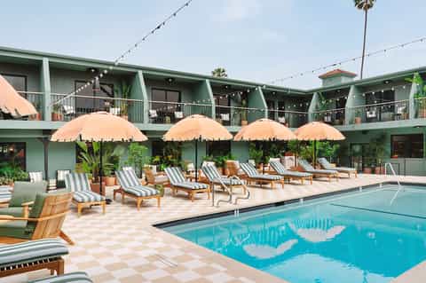 Resort pool with peach umbrellas, striped loungers, green building facade, and string lights