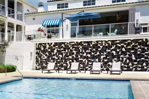 Modern beach house with white exterior, black and white tile wall, pool and blue umbrella