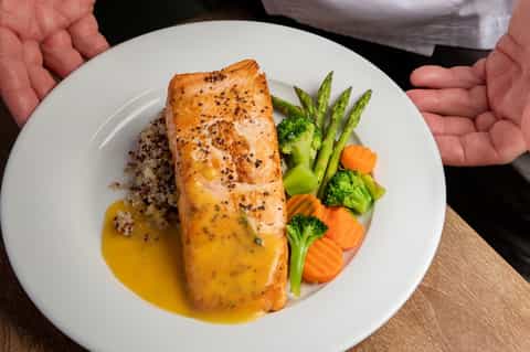 Plated salmon with quinoa, asparagus, carrots, and lemon sauce presented by server