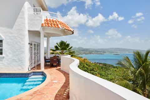 White Mediterranean villa with private curved pool, ocean views, palm trees, and dramatic coastal landscape