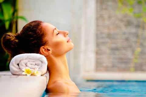 Woman relaxing in pool with rolled towel and yellow flower spa amenity
