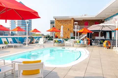 Resort pool deck with bright red and orange umbrellas, loungers, colorful play areas, and contemporary architecture