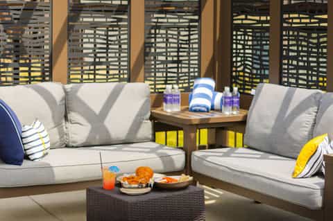Outdoor lounge area with gray cushioned seating, striped pillows, wooden table, and slatted privacy screens