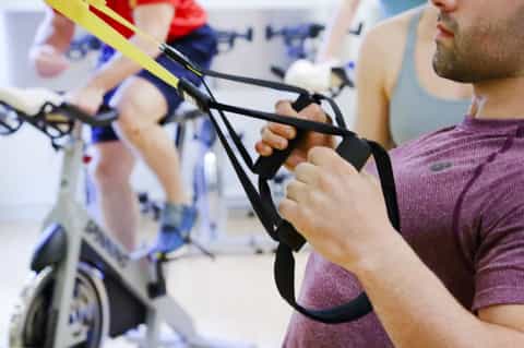 Man holding TRX suspension training straps with fitness class participants in background